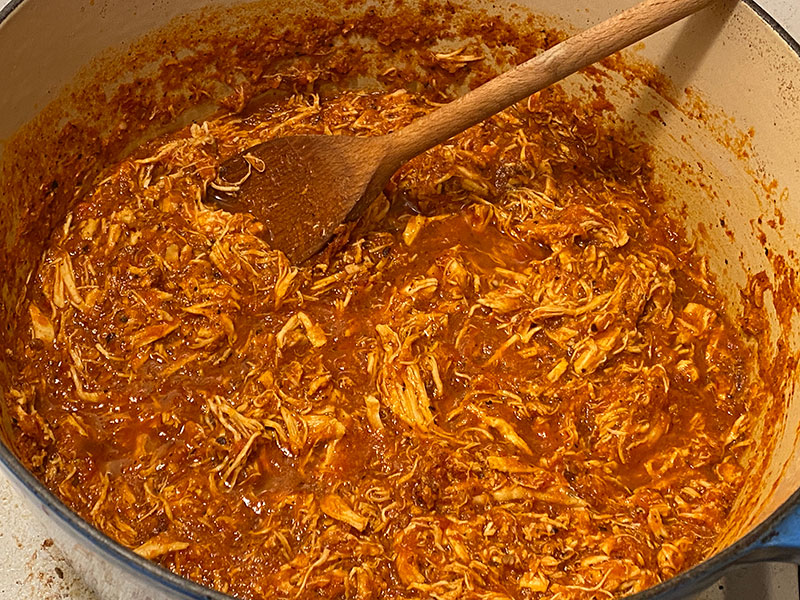 A big Le Creuset filled with chicken tinga meat finished simmering and reducing the volume of chicken stock