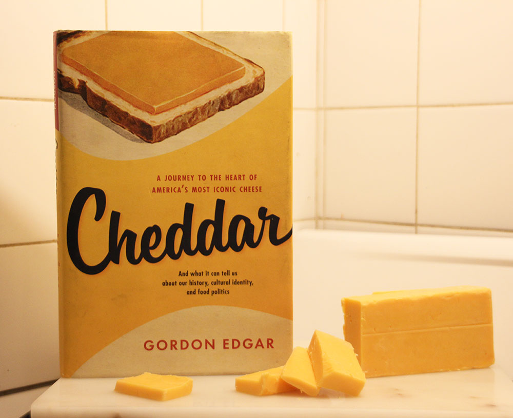 The book, Cheddar, by Gordon Edgar, sits beside yellow block cheddar on a white stove
