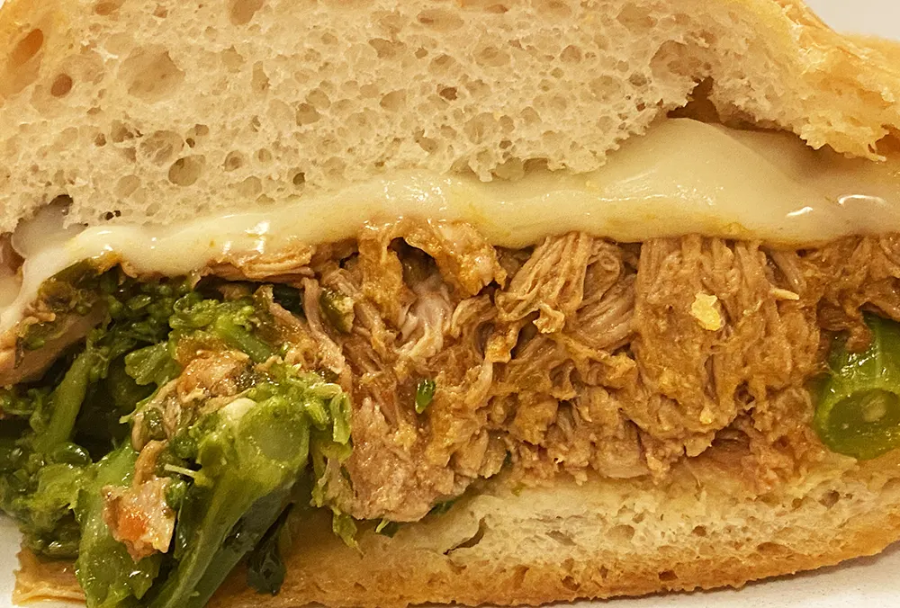 A cross section of the  Philadelphia Italian pork sandwich showing layers of bread, cheese, meat, broccoli rabe, and more bread